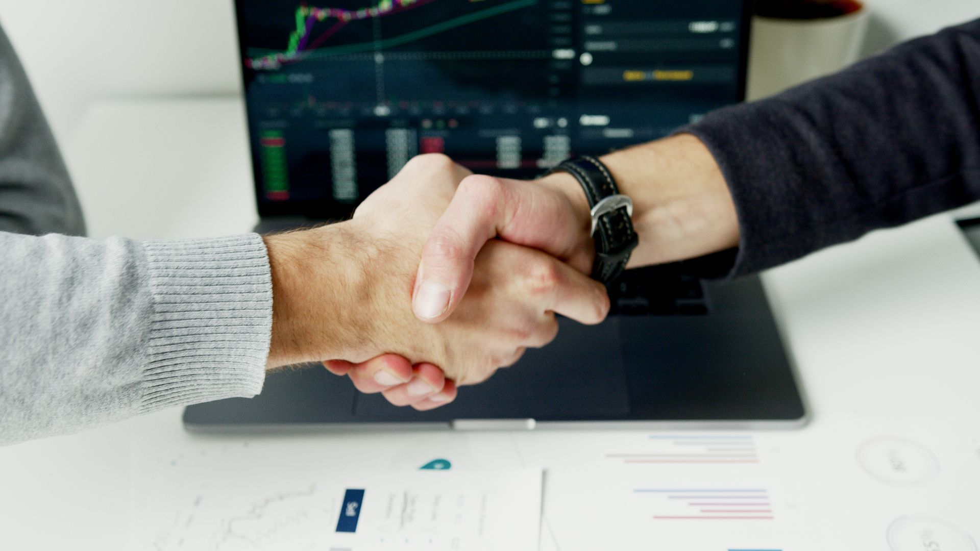 A firm handshake over a laptop — partnership sealed